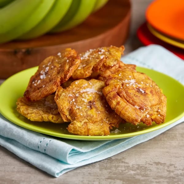 A vibrant green plate piled high with golden-brown, crispy Jamaican tostones, sprinkled with sea salt.
