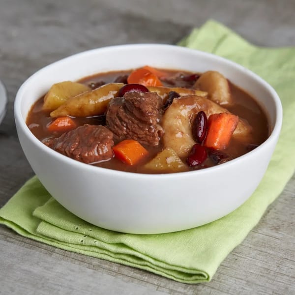 A white bowl of Jamaican beef stew with carrots, potatoes, and beans on a green napkin.