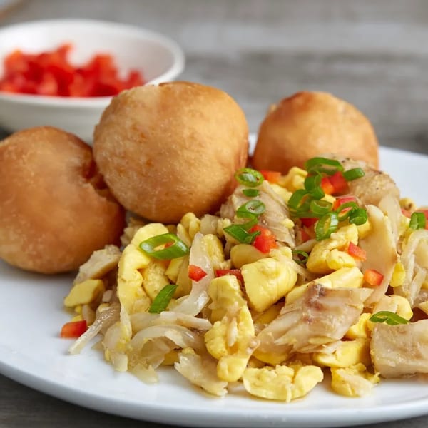 A plate of Jamaican ackee and saltfish with fried dumplings, garnished with scallions and red peppers.