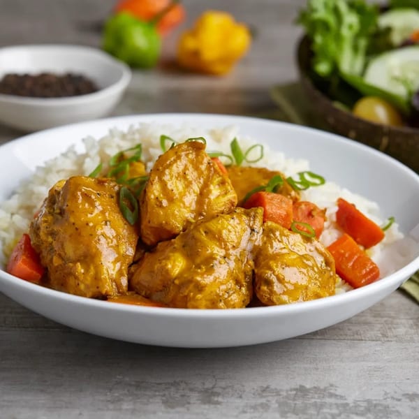 A white bowl of Fiery Irie Jamaican curry chicken with rice, carrots, and green onions.